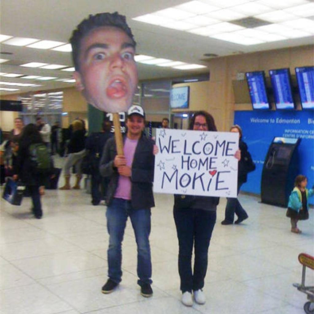 Two people holding funny airport greeting signs.