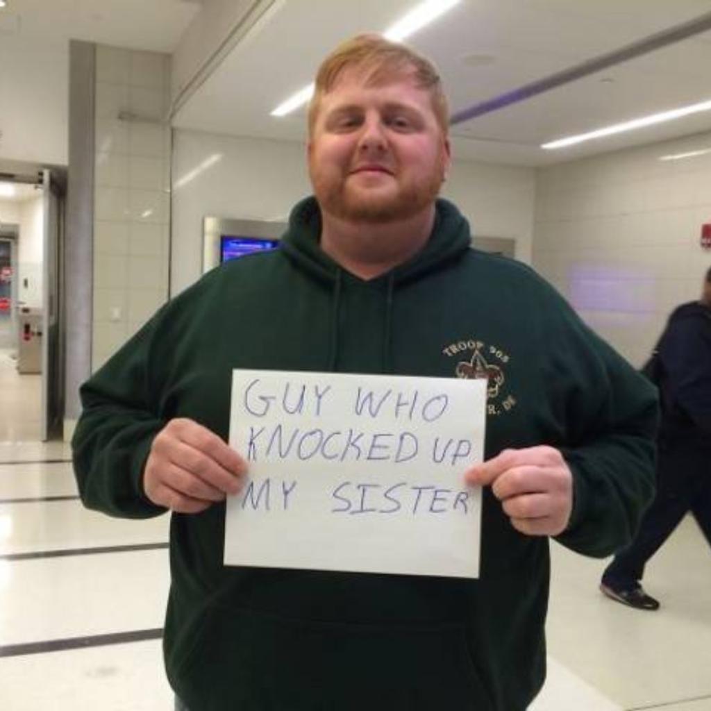 A man holding a funny airport greeting sign.