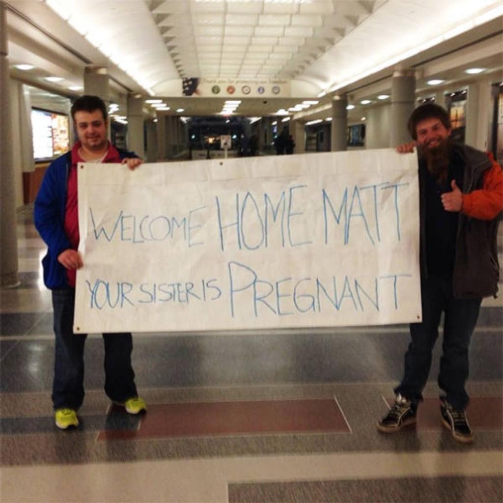 Two men holding a funny airport greeting sign.